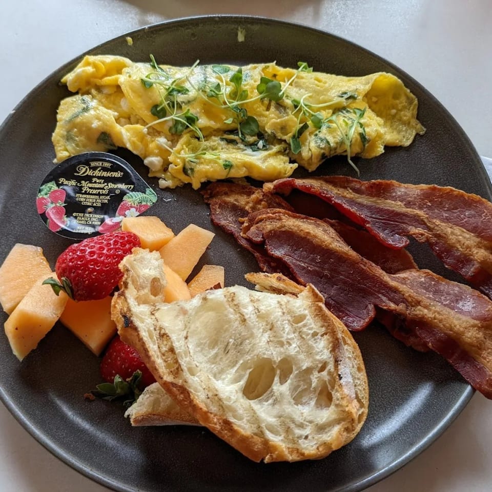 Banyan Kitchen's breakfast plate with omelet, bacon, fruit, bread, and strawberry preserves.