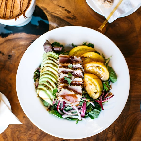 Seared tuna salad with avocado, yellow tomatoes, and red onion on a white plate.