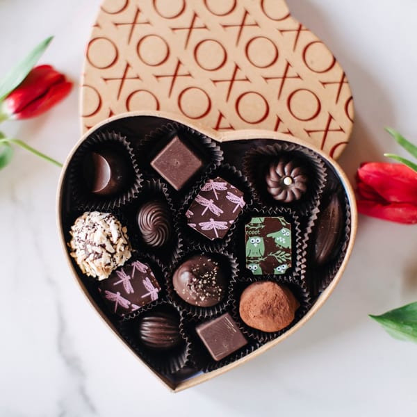 Heart-shaped box of assorted chocolates with red tulips on a white marble surface.