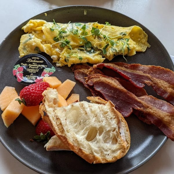 Banyan Kitchen's breakfast plate with omelet, bacon, fruit, bread, and strawberry preserves.