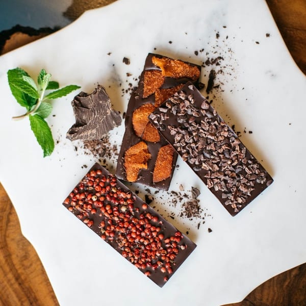 Three dark chocolate bars with various toppings, mint, and chocolate shavings on a white surface.