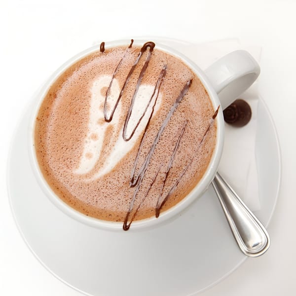 Overhead view of a Banyan Kitchen hot chocolate with chocolate drizzle and a small chocolate candy.