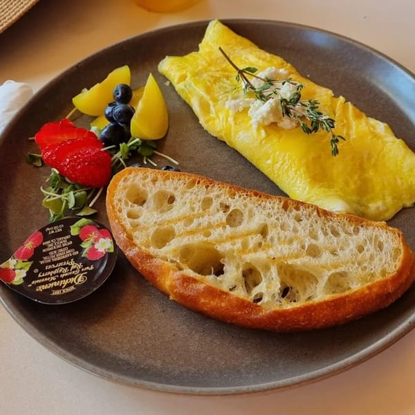 A Banyan Kitchen breakfast plate with a fluffy omelet, fresh fruit, toasted bread, and raspberry preserves.