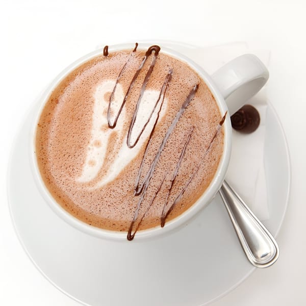 Overhead view of a Banyan Kitchen cafe mocha with chocolate drizzle, a spoon, and a chocolate candy.