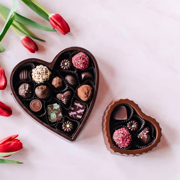 Two heart-shaped boxes of assorted chocolates and red tulips on a light pink surface.